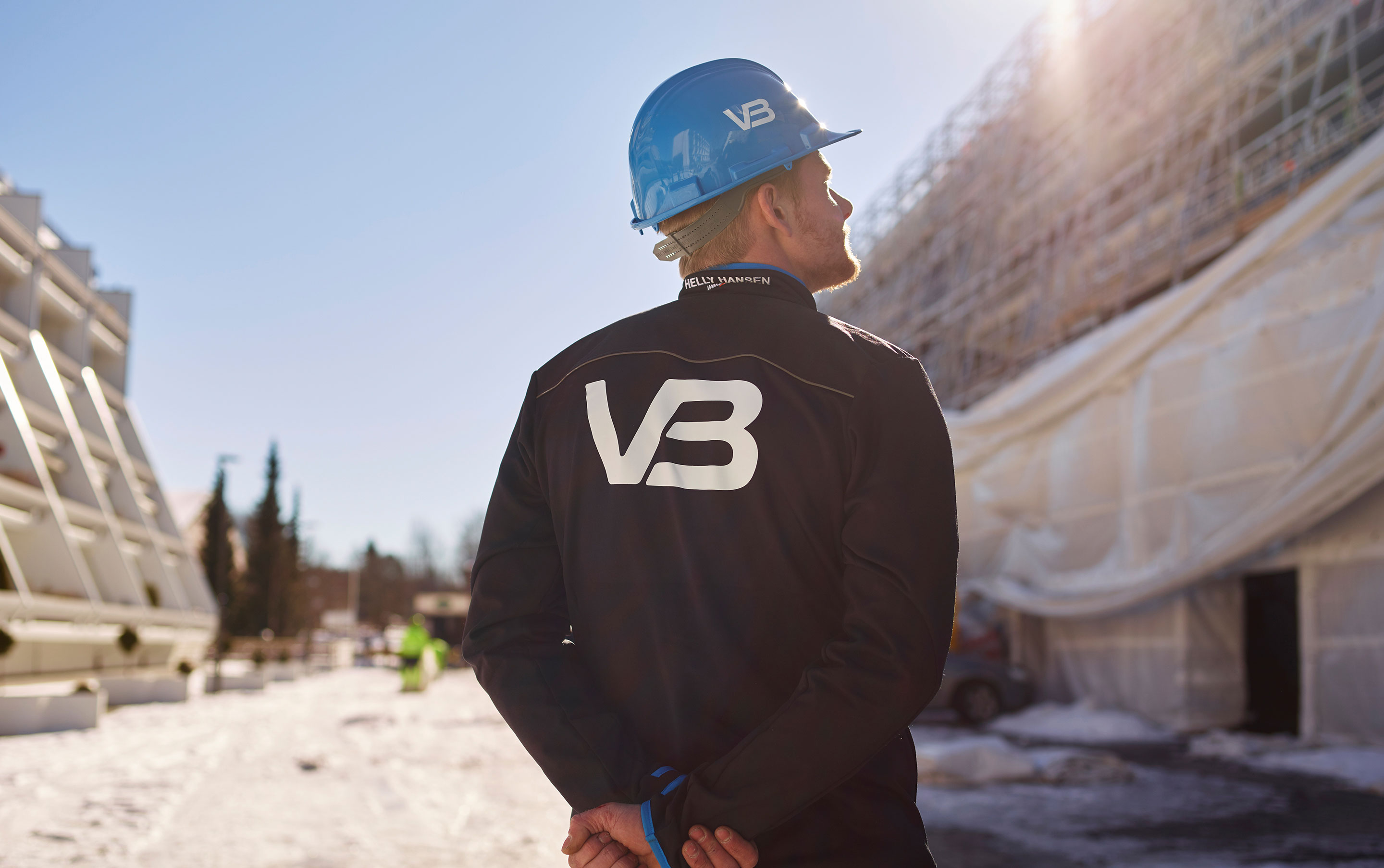VB-rørlegger med logo på jakke og hjelm, på byggeplass.